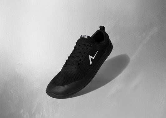 Black sneaker with a white logo on a light gray background. High fashion barefoot shoe built for durable workouts, Training never looked this good. Feet get 60% stronger with wearing these barefoot shoes.