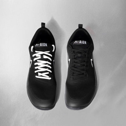 Black athletic shoes with white laces on a light gray background. The best barefoot shoe in the game. Wide toe box flexible sole and the durability to last a long time under strain and load.